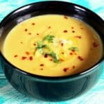 Easy Homemade Acorn Squash Soup Served in a Black Ceramic Bowl, and garnished with red pepper flakes and cilantro.