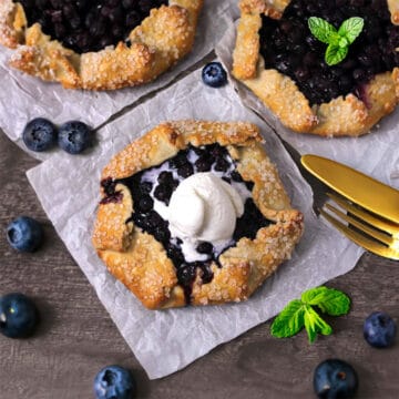 Quick and delicious mini blueberry galettes or crostatas on white parchment paper.