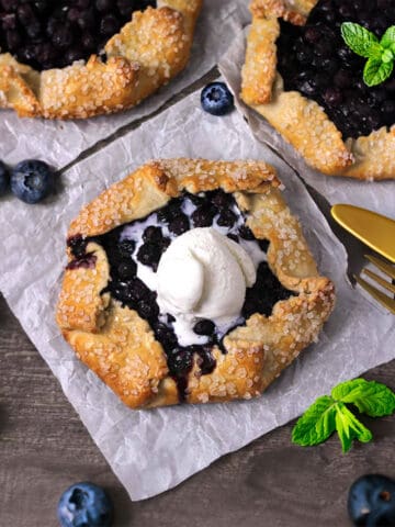 Quick and delicious mini blueberry galettes or crostatas on white parchment paper.