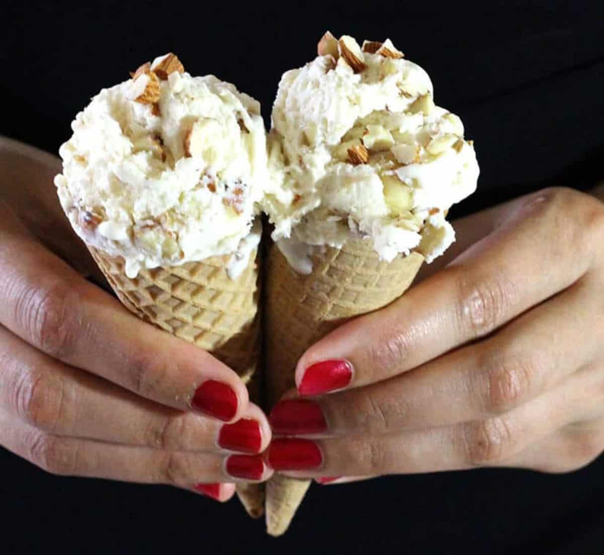 Scoops of delicious homemade roasted almond ice cream in two waffle cones held in hand.