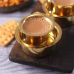 Best Indian tea (authentic homemade chai or milk tea) on a golden serving cup with biscuits.