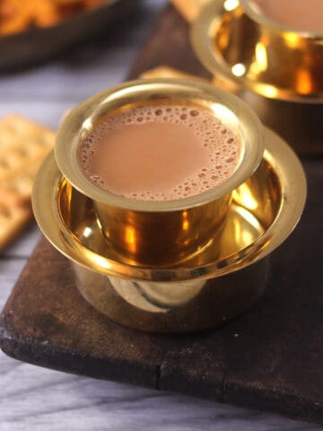 Best Indian tea (authentic homemade chai or milk tea) on a golden serving cup with biscuits.