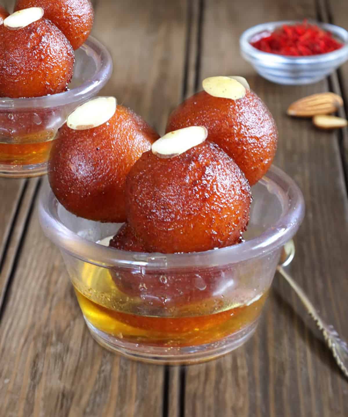 Nest homemade gulab jamun served in glass bowls with saffron-flavored sugar syrup.