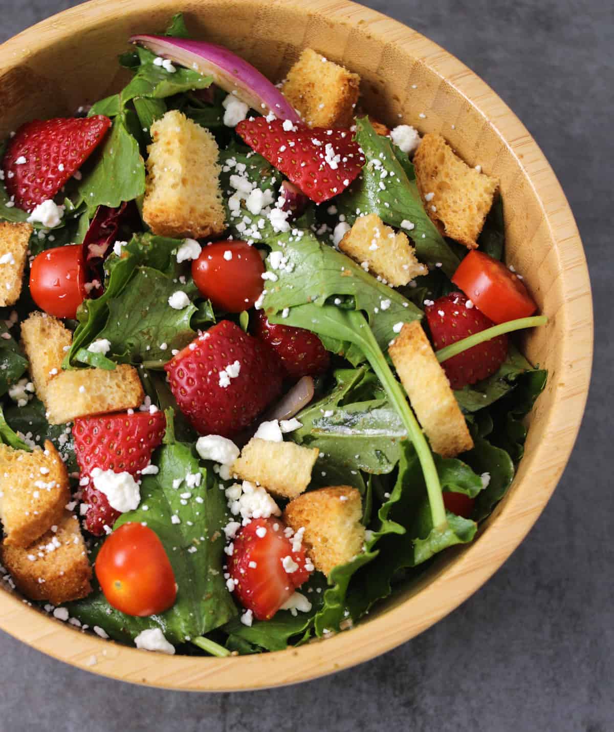 Summer salad bowl with fresh strawberries, greens like spinach and arugula, feta, and easy dressing.